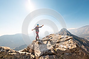 young girl climber in a helmet and with a backpack walks along a mountain range against the backdrop of mountains and climbing and