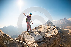 young girl climber in a helmet and with a backpack walks along a mountain range against the backdrop of mountains and climbing and