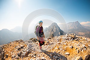 young girl climber in a helmet and with a backpack walks along a mountain range against the backdrop of mountains and climbing and