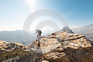 young girl climber in a helmet and with a backpack walks along a mountain range against the backdrop of mountains and climbing and