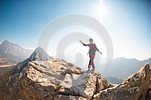 young girl climber in a helmet and with a backpack walks along a mountain range against the backdrop of mountains and climbing and