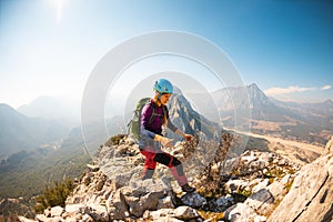 young girl climber in a helmet and with a backpack walks along a mountain range against the backdrop of mountains and climbing and