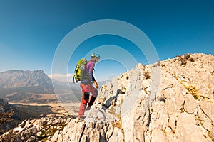 young girl climber in a helmet and with a backpack walks along a mountain range against the backdrop of mountains and climbing and