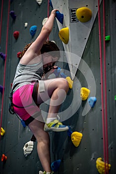 Young girl climbing up on practice wall in indoor rock gym