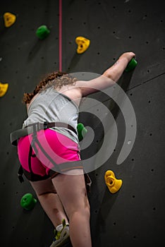 Young girl climbing up on practice wall in indoor rock gym