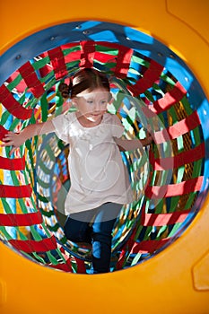 Young girl climbs through netted tunnel in soft play centre