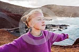 Young girl with closed eyes enjoing sea wind blowing in face. Smilling blonde girl enjoying nature of Canary islands