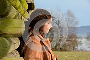 Young girl with closed eyes,  leans against a wooden lodge