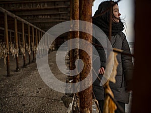 Young girl in a coat stands near metal rusty structures near the sea coast