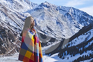 Young girl in colorful blanket on winter snowy mountains background.