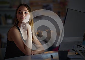 Young girl with computer sitting at desk at night, online dating concept.