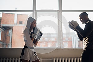 A young girl conducts kickboxing training and practices paw strikes with a professional boxer