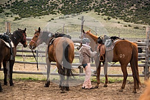 Young girl in corral saddling her horse for a trailride