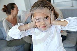 Young girl covering ears, parents arguing
