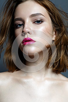 A young girl with crimson lips and fluttering hair. Beautiful model with makeup nude and shining skin. Photo taken in the studio.