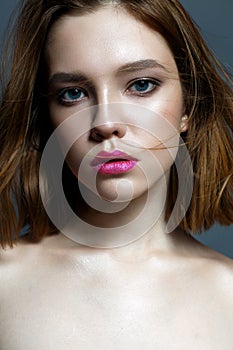 A young girl with crimson lips and fluttering hair. Beautiful model with makeup nude and shining skin. Photo taken in the studio.