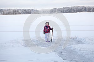 Young girl with crowbar in hand standing near cleared ice on lake for making ice-hole