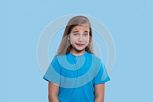 Young girl  crys with grief covering your mouth with palms against blue background in studio