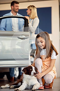 Young girl cuddling dog while mother bying a new car photo