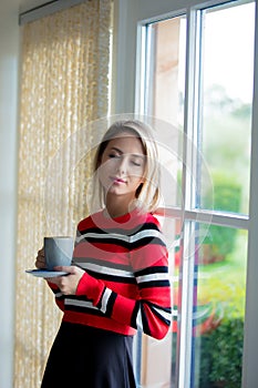 Young girl with cup of coffee stay near window
