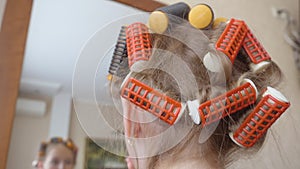 Young girl with curlers on hair applying makeup cream front mirror back view