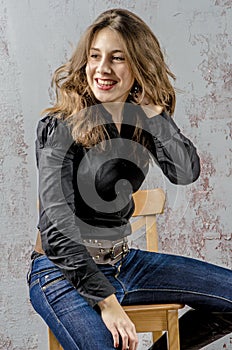 Young girl with curly hair in a black shirt, jeans and high boots cowboy western style