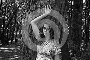 A young girl with curly hair stands near a tree with a wide trunk. Summer walk in the Park.