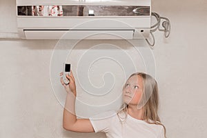 Young girl cute blonde teenager of European appearance holds in his hands a remote control of air conditioning in the interior of