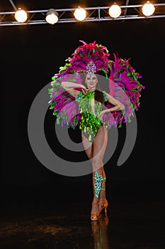 A young girl dancer of European appearance on stage in a carnival costume of green and pink feathers