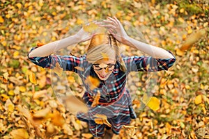 Young girl dancing under falling leaves in the autumn park