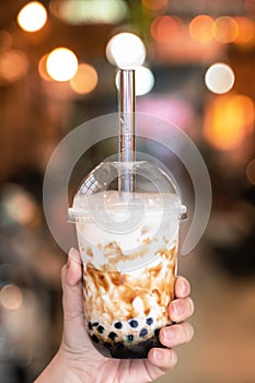 Young girl in denim jacket is drinking brown sugar flavored tapioca pearl bubble milk tea with glass straw in night market of