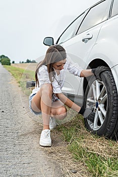 young girl is disappointed by a car breakdown, a flat tire and its replacement on the road