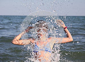 Young girl in diving mask plays by spraying sea water in the air