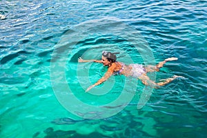 Young girl with diving mask and snorkel dives in clear blue sea water, adult woman in white bikini swims in turquoise clean water