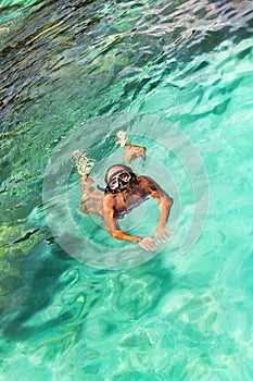 Young girl with diving mask and snorkel dives in clear blue sea water, adult woman in white bikini swims in turquoise clean water