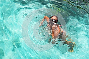 Young girl with diving mask and snorkel dives in clear blue sea water, adult woman in white bikini swims in turquoise clean water