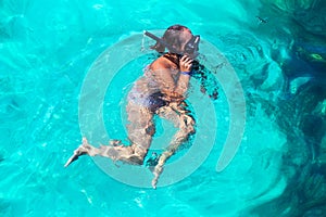 Young girl with diving mask and snorkel dives in clear blue sea water, adult woman in white bikini swims in turquoise clean water