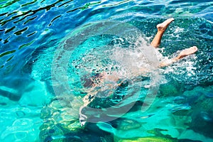 Young girl with diving mask and snorkel dives in clear blue sea water, adult woman in white bikini swims in turquoise clean water