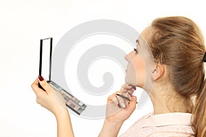 Young girl does a makeup in front of a small cosmetic mirror.