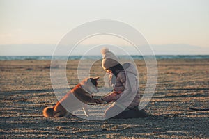 A young girl with a dog in nature. Kid girl playing with a shiba inu dog on the beach at sunset in Greece in winter