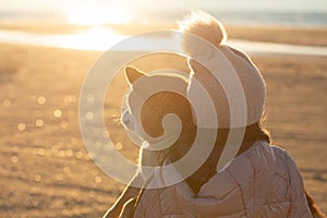 A young girl with a dog in nature. Kid girl sitting with a shiba inu dog on the beach at sunset in Greece in winter