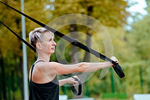 Young girl doing exercises outdoors, holds TRX loop/