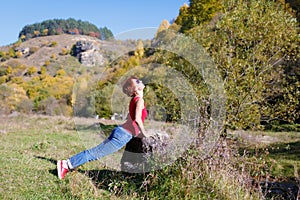 Young girl doing exercises on the river coast against the background of mountains and forest