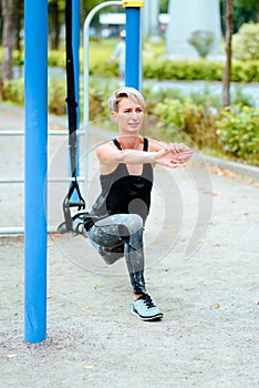 Young girl doing lunge to the side in the park. Uses TRX