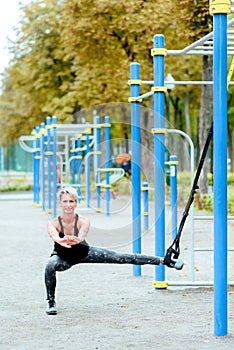 Young girl doing lunge to the side in the park. Uses TRX