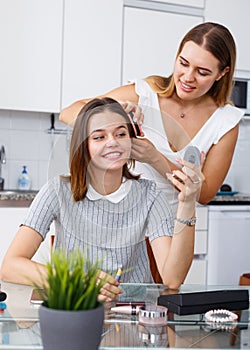 Young girl doing make-up at table and girlfriend combing her hair