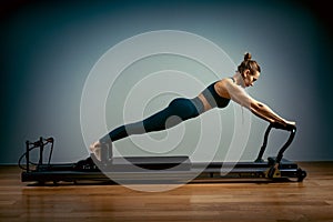 Young girl doing pilates exercises with a reformer bed. Beautiful slim fitness trainer on reformer gray background, low photo