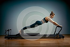 Young girl doing pilates exercises with a reformer bed. Beautiful slim fitness trainer on reformer gray background, low