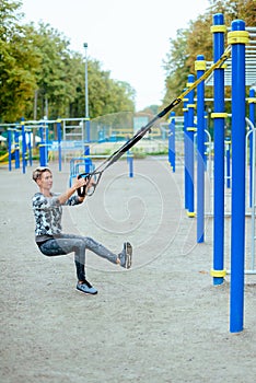 Young girl doing sports on a playground  using slings, TRX loop
