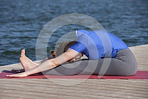 Young girl doing yoga or fitness exercise outdoor in nature with beautiful lake. Meditation and Relax concept